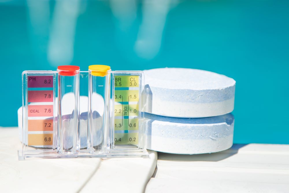Chlorine shock tablets and pH balancing test kits sitting outside on the ledge of a pool.